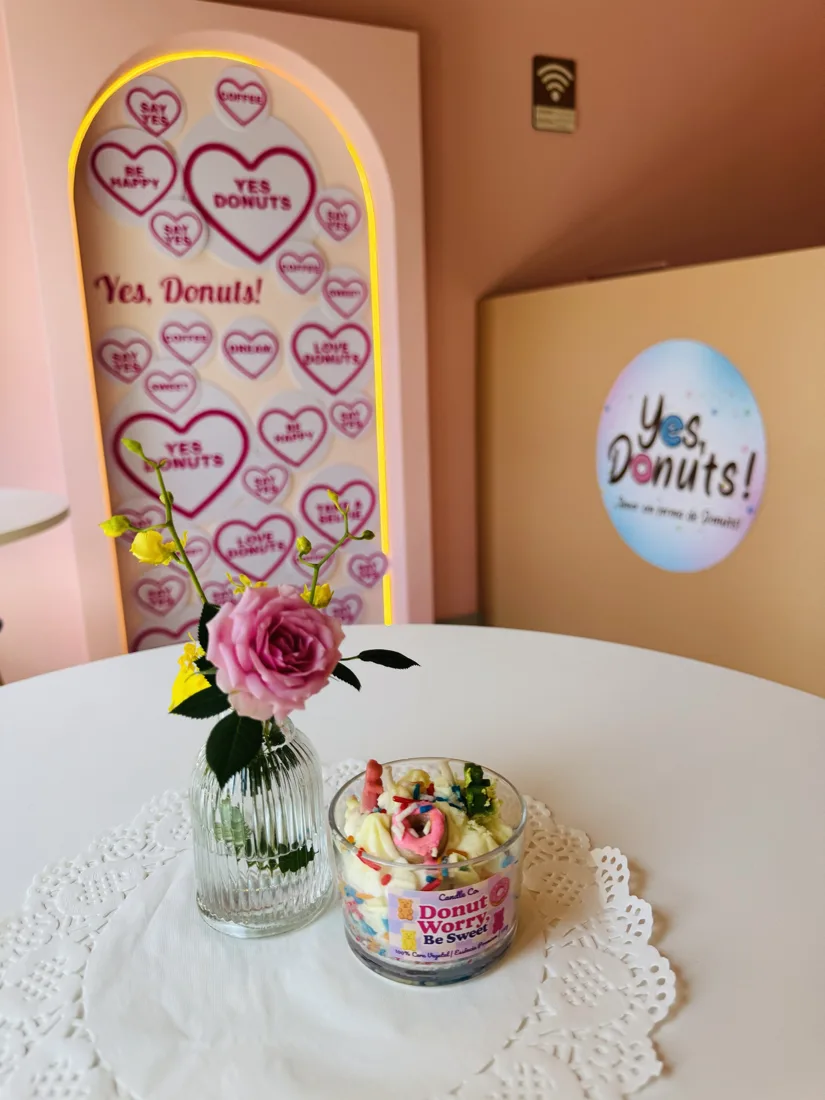 Mesa com rosa em vaso de vidro e toalhinha de renda, com o painel de corações ao fundo