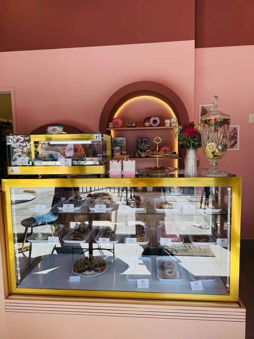 Vitrine dourada com os donuts do dia e nicho iluminado com xícaras e decoração